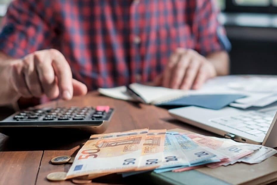 Taschenrechner, Euro-Scheine und Münzen vor arbeitendem Mann – Symbolbild für niedrige Rente auf Bürgergeld-Niveau nach 30 Jahren Arbeit