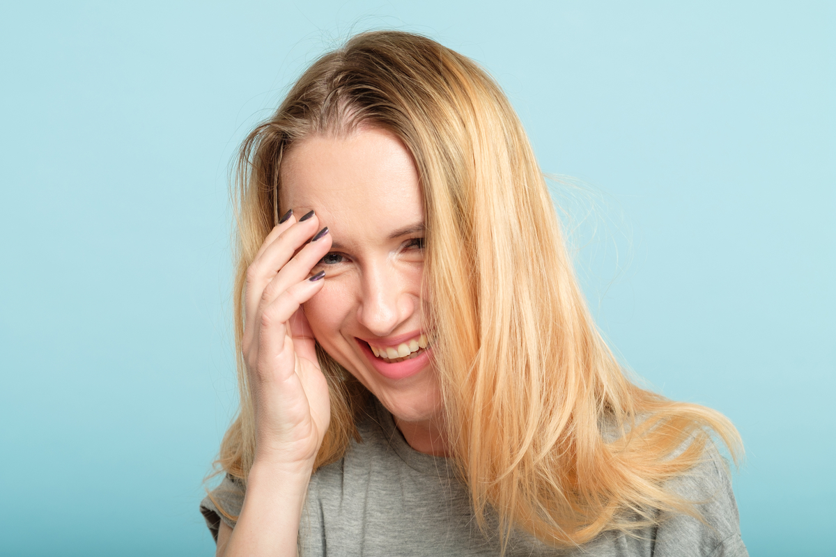 blonde Frau fasst sich lachend ins Gesicht Face Palm
