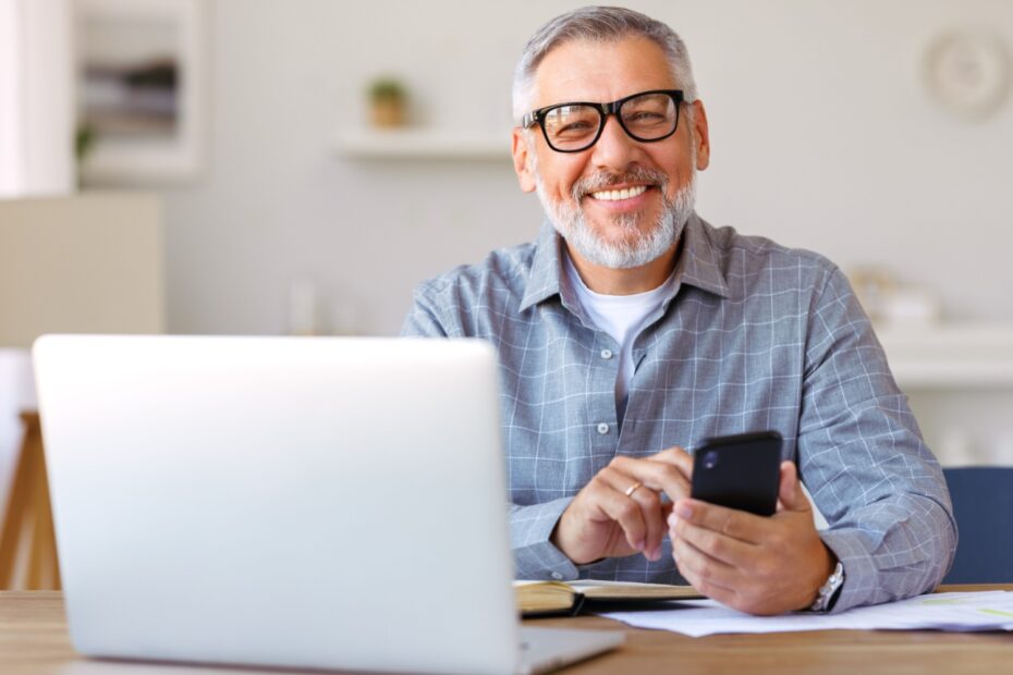 Rentner sitzt am Tisch vor einem Laptop und freut sich