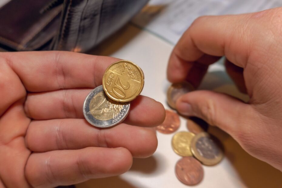 Hände zählen Euro-Münzen über einer leeren Geldbörse, um den geringen Zuverdienst beim ALG 1 zu symbolisieren.