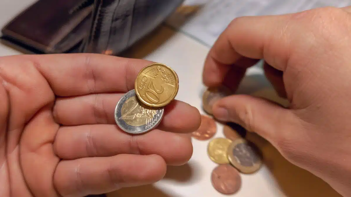 Hände zählen Euro-Münzen über einer leeren Geldbörse, um den geringen Zuverdienst beim ALG 1 zu symbolisieren.