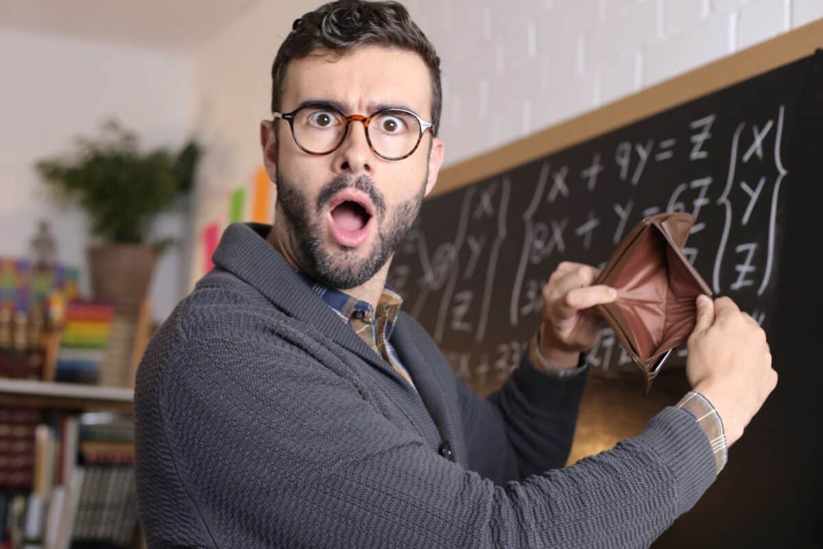 Junger Lehrer hält empört leere Geldbörse hoch, Symbol für Arbeitslosigkeit