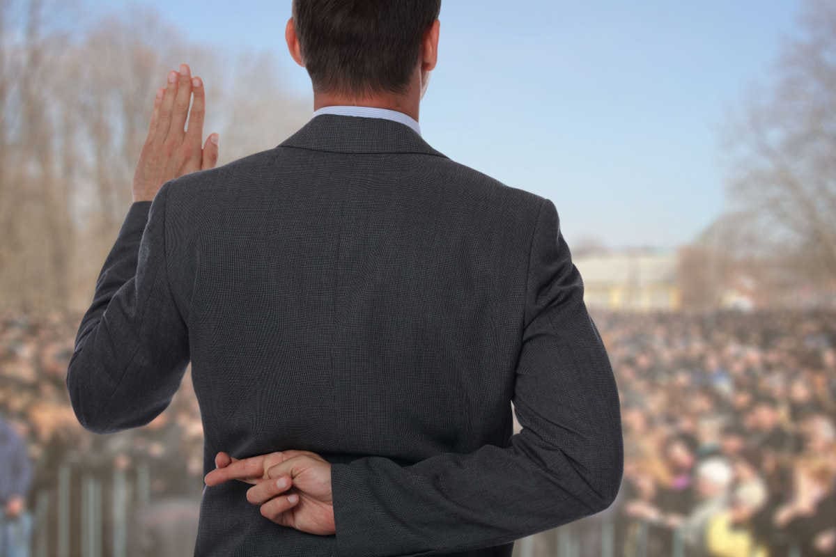 Politiker schwört vor Menschenmenge und kreuzt hinter dem Rücken die Finger