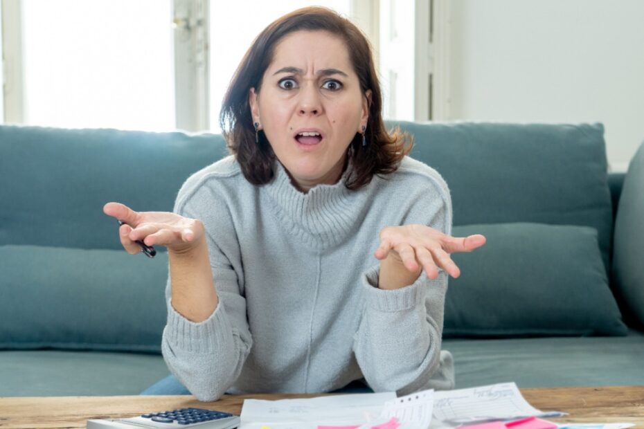Frustrierte Frau mit Taschenrechner und Papieren am Tisch. Sie drückt Verwirrung oder Ärger über finanzielle Probleme und Bürokratie (Jobcenter/Bürgergeld-Bescheide) aus.