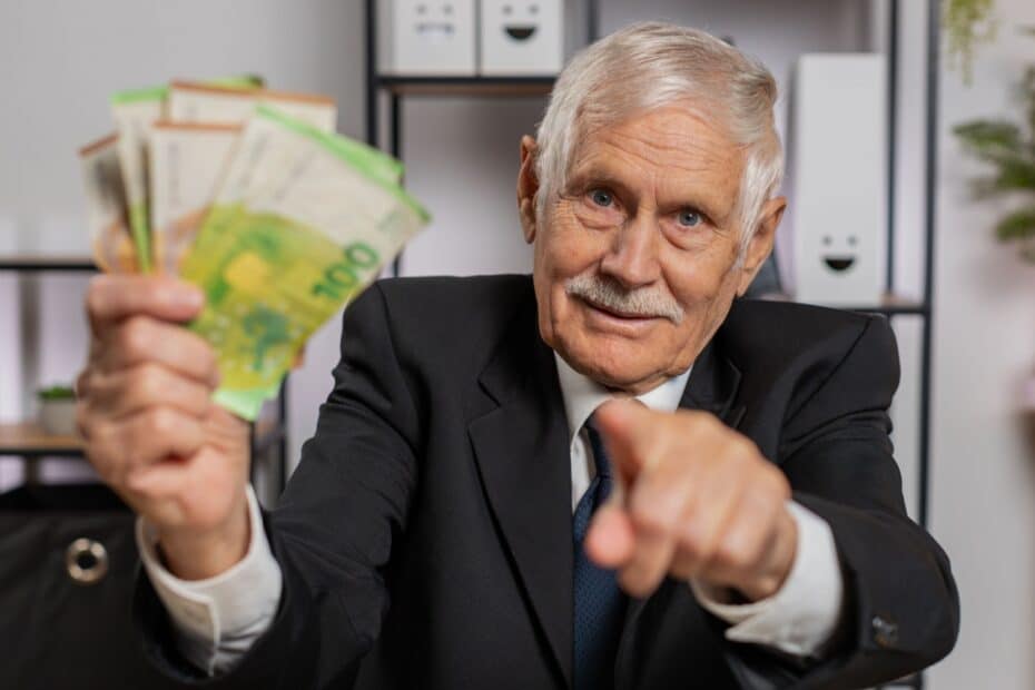 Rentner hält einige Euro-Gelscheine hoch und zeigt mit der anderen Hand richtung Betrachter, symbolisch für Boomer-Soli der Rente