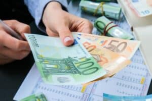 Hand reicht über dem Schreibtisch einige Geldschreine, symbolisch für Vorschuss vom Chef