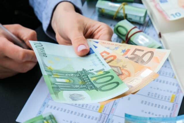 Hand reicht über dem Schreibtisch einige Geldschreine, symbolisch für Vorschuss vom Chef