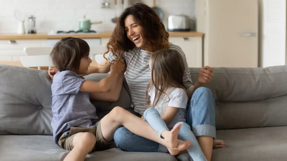 Lachende alleinerziehende Mutter spielt mit ihren zwei Kindern im Wohnzimmer.