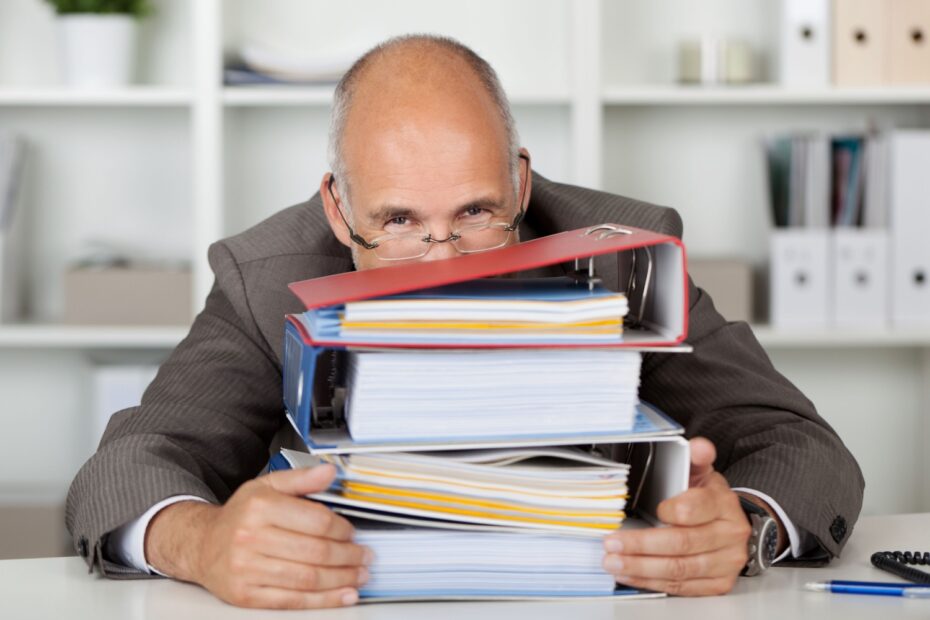 Mann im Büro versteckt sein grinsendes Gesicht hinter Aktenordnern