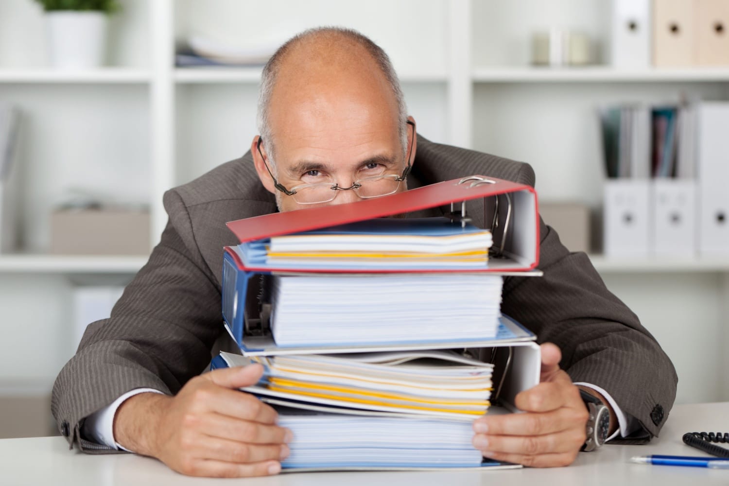 Mann im Büro versteckt sein grinsendes Gesicht hinter Aktenordnern