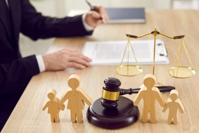 Holz‑Familienfiguren, Richterhammer und Waage auf Schreibtisch – Symbol für Bürgergeld‑Ansprüche im Wechselmodell