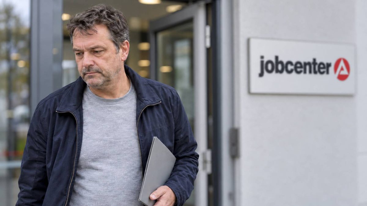 Mann mit Dokumentenmappe verlässt unzufrieden ein Jobcenter.