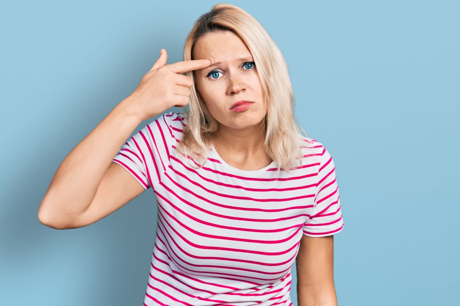 Junge Frau tippt sich ungläubig mit dem Finger auf die Stirn