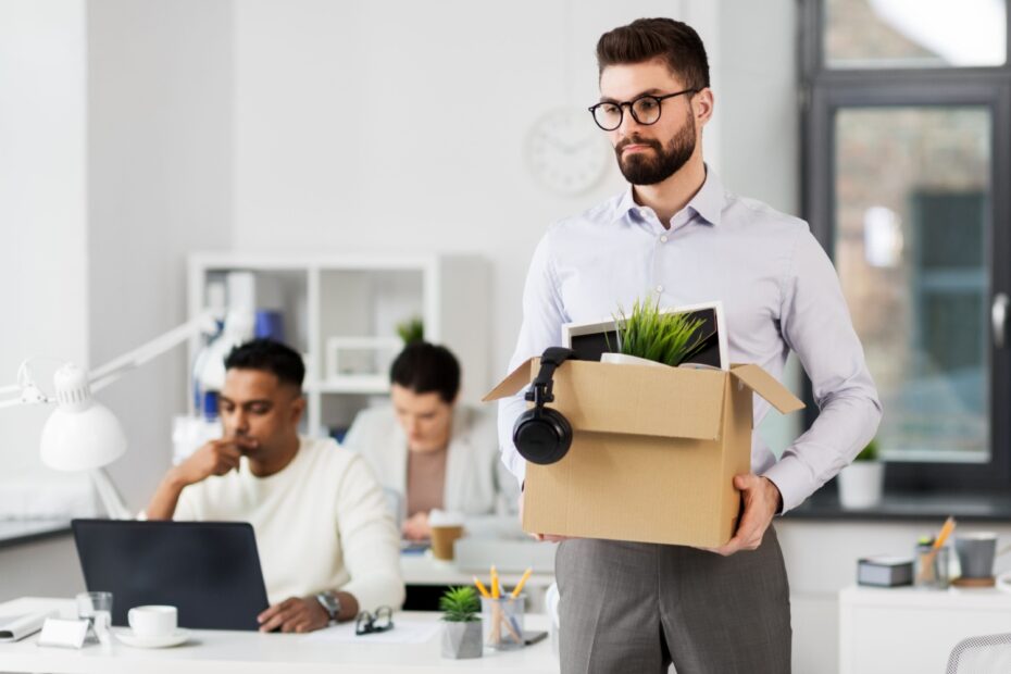 Man verlässt mit gepackter Schachtel seinen Arbeitsplatz, symbolisch für Kündigung