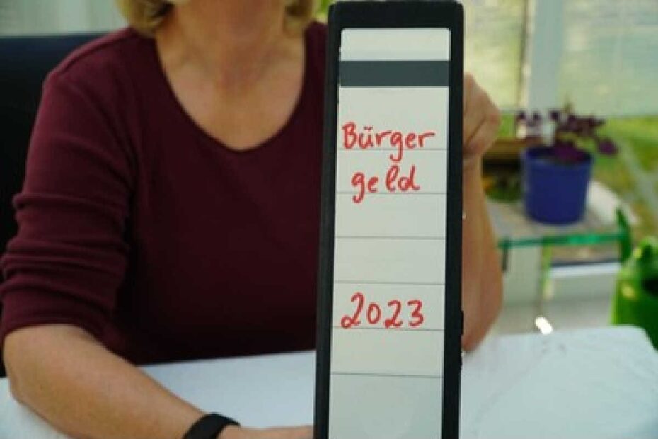 Sachbearbeiterin hält Ordner mit Aufschrift Bürgergeld 2023 hoch
