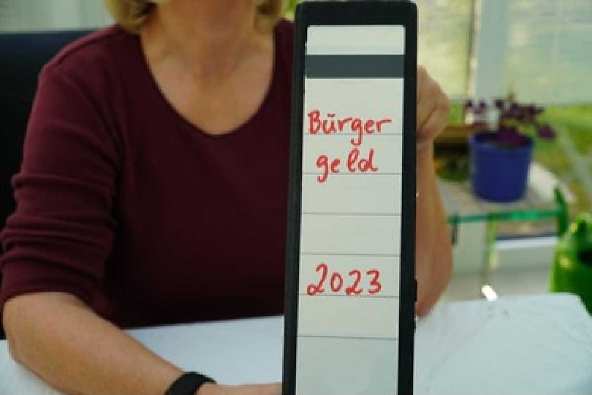 Sachbearbeiterin hält Ordner mit Aufschrift Bürgergeld 2023 hoch
