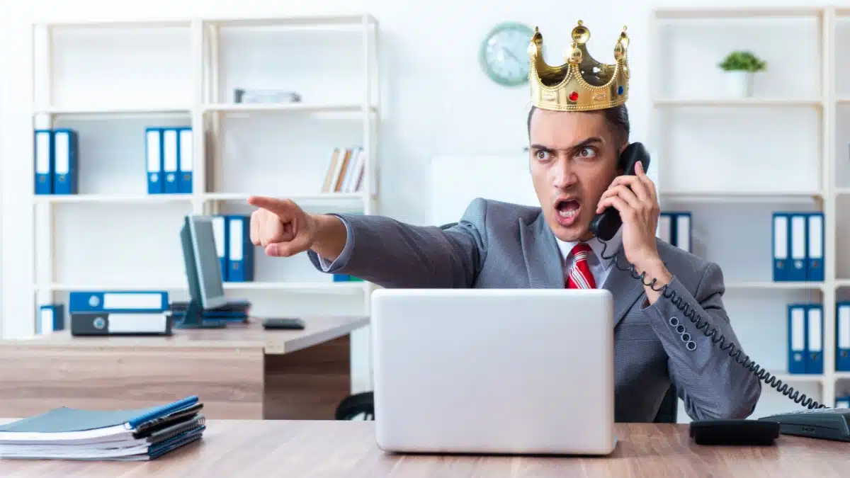 Satirische Darstellung eines wütenden, autoritären Jobcenter-Mitarbeiters (Sachbearbeiter) mit goldener Königskrone, der schreiend telefoniert und mit dem Finger Befehle erteilt.
