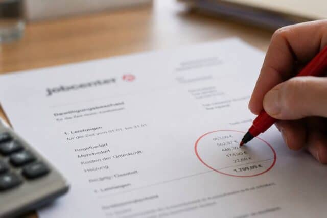 Hand mit rotem Stift markiert eine Zahl auf einem Bewilligungsbescheid des Jobcenters