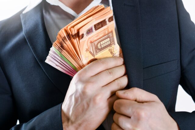 Mann versteckt heimlich Bündel von Euro-Scheinen in seinem Sakko, Symbol für Bürgergeld-Betrug