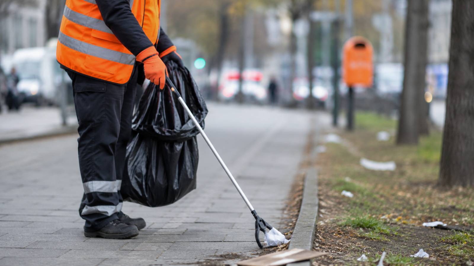 Eine Person in Warnweste sammelt mit einem Greifwerkzeug Müll auf einem Gehweg.