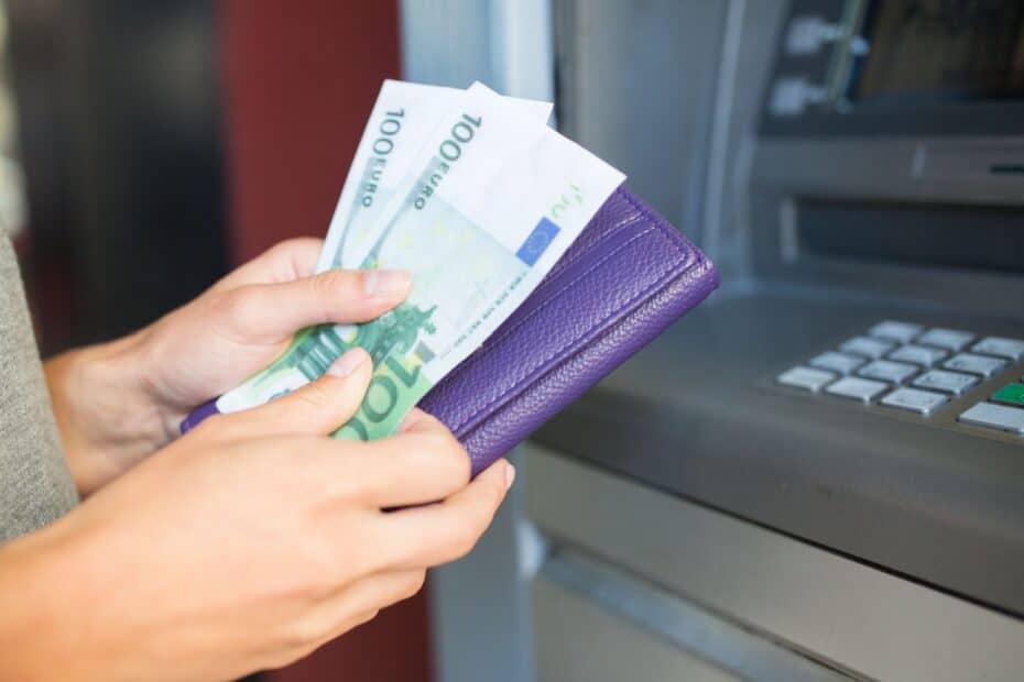 Weibliche Hände halten Geldscheine und Portemonnaie vor einem Geldautomaten