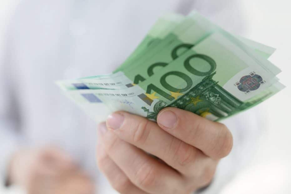 Hand hält Euro-Scheine (überwiegend 100 Euro) vor hellem Hemd – Bürgergeld Auszahlung