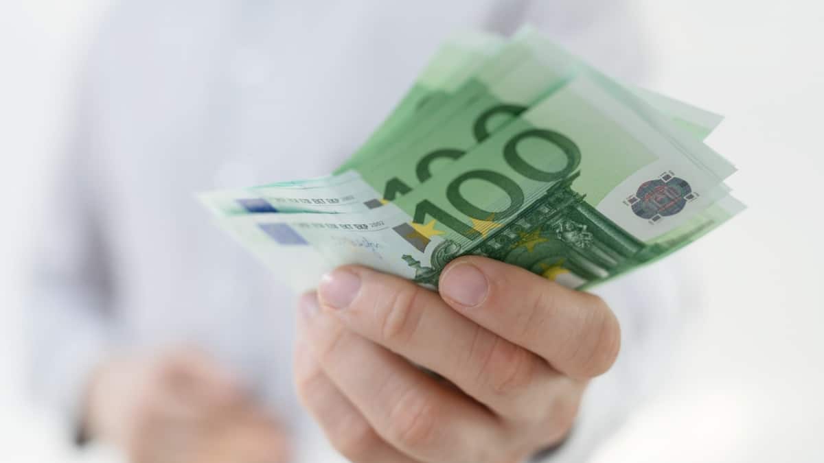 Hand hält Euro-Scheine (überwiegend 100 Euro) vor hellem Hemd – Bürgergeld Auszahlung