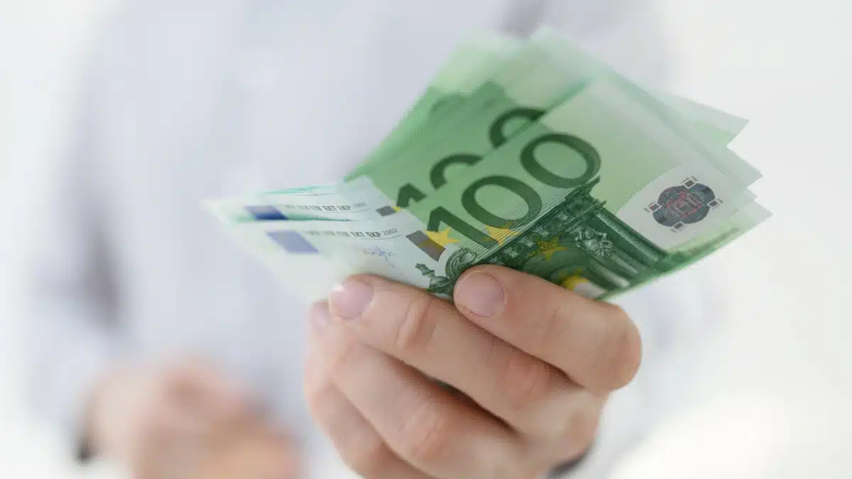 Hand hält Euro-Scheine (überwiegend 100 Euro) vor hellem Hemd – Bürgergeld Auszahlung