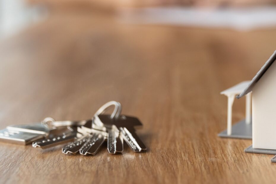 Hausschlüssel auf dem Tisch neben einem Modell-Haus, symbolisch für Hauskauf