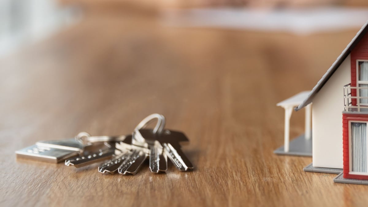 Hausschlüssel auf dem Tisch neben einem Modell-Haus, symbolisch für Hauskauf