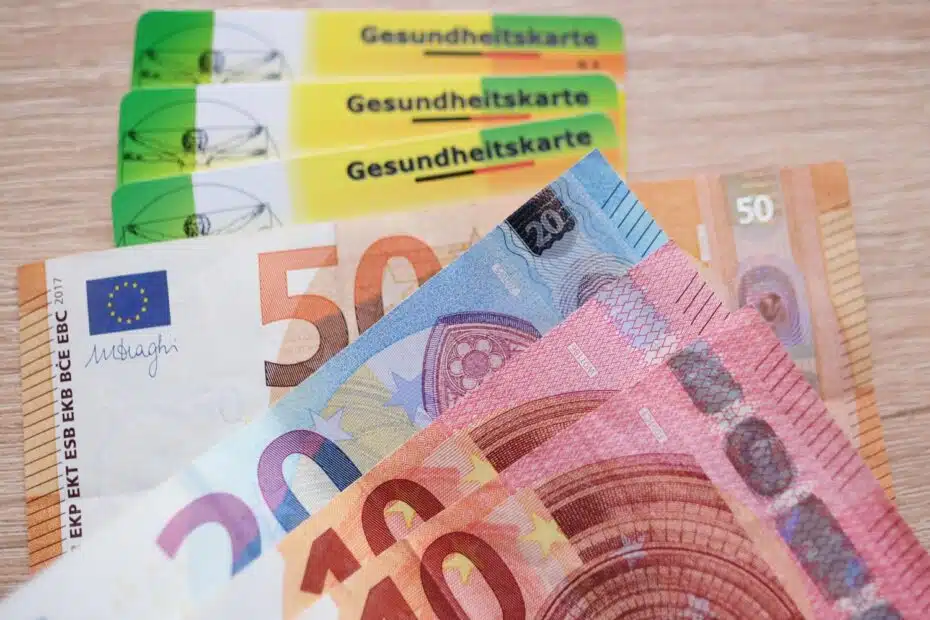 Euro-Geldscheine auf Stapel von Krankenkassenkarten der GKV
