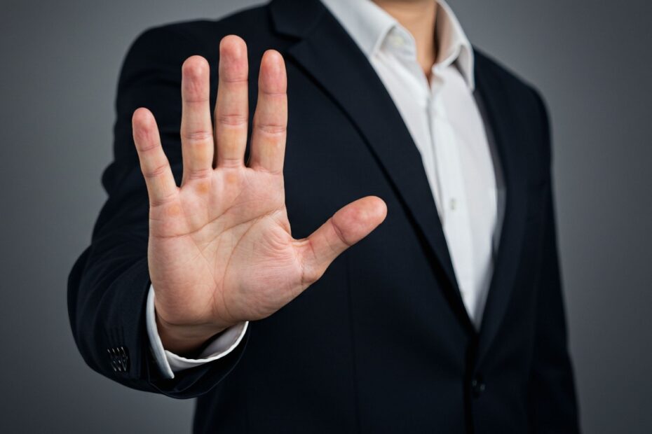 Symbolbild zur harten Linie beim Bürgergeld: Eine abwehrende Stopp-Handgeste eines Mannes im Business-Anzug vor grauem Hintergrund, die den Entzug von Sozialleistungen verdeutlicht.