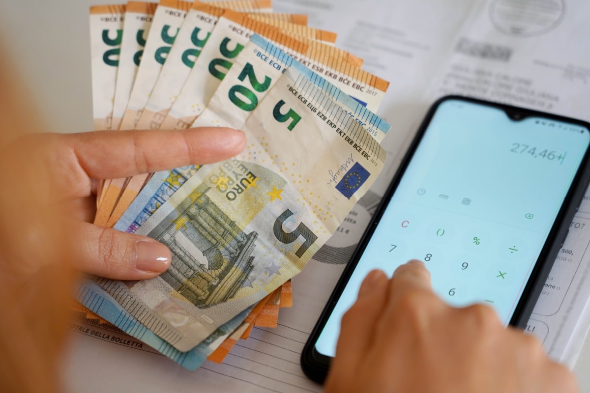 Frau zählt Geldscheine und rechnet mit Handy-Taschenrechner nach.