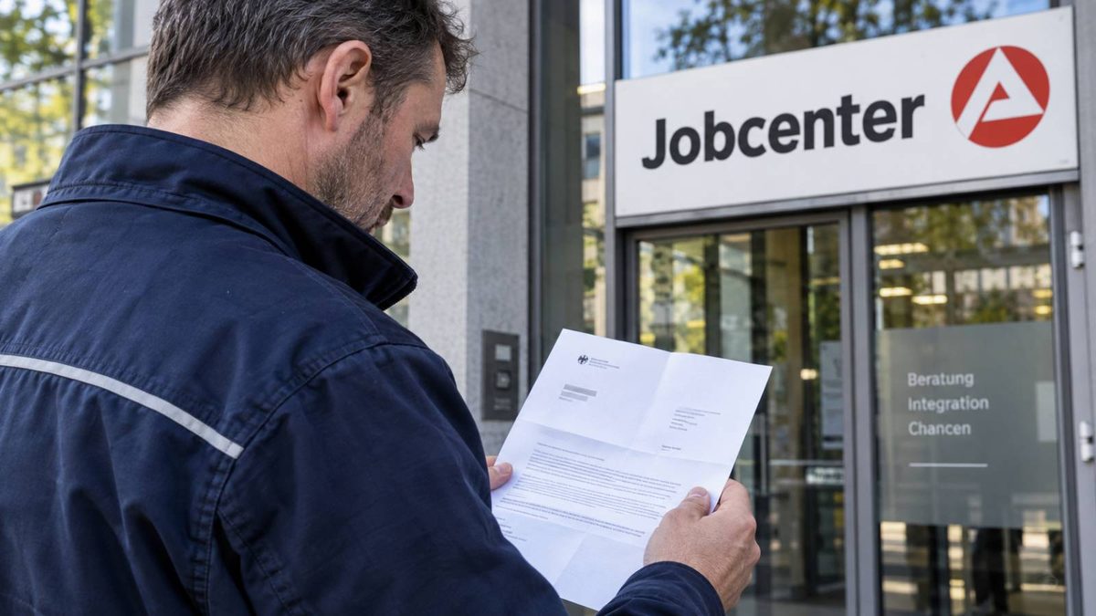 Mann in Arbeitskleidung liest einen Brief vor dem Eingang eines Jobcenters.