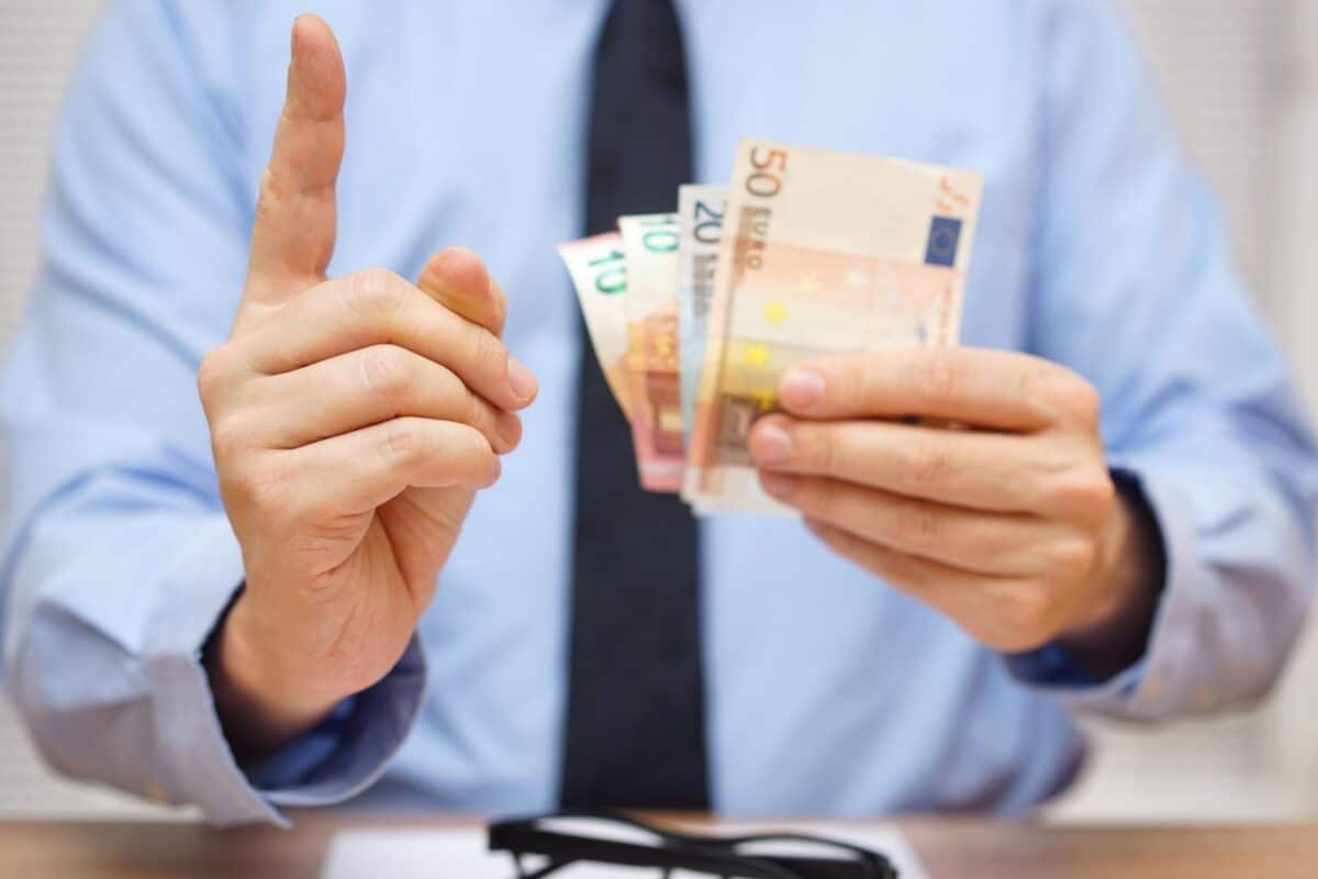 Mann mit Krawatte und erhobenen Zeigefinger hält einige Geldscheine