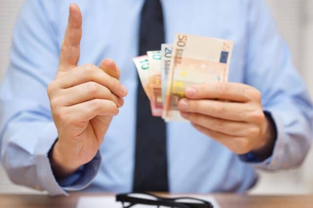 Mann mit Krawatte und erhobenen Zeigefinger hält einige Geldscheine