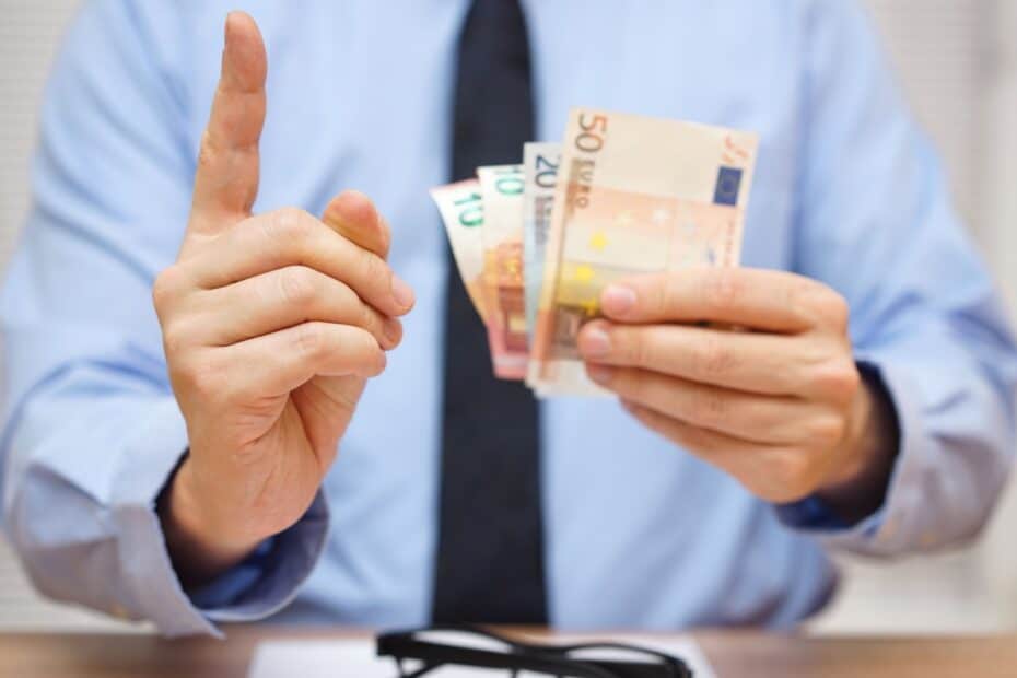 Mann mit Krawatte und erhobenen Zeigefinger hält einige Geldscheine