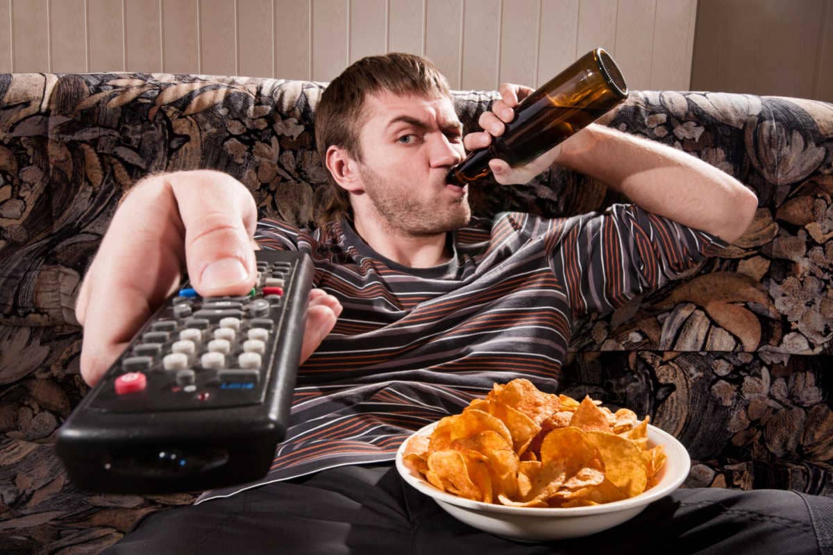 Junger Mann mit Bier und Chips auf dem Sofa beim TV