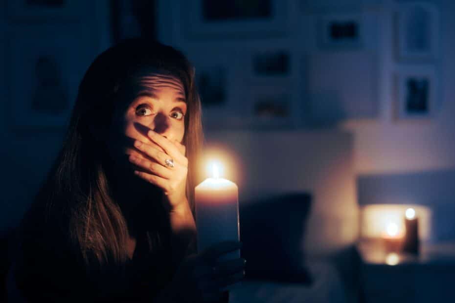Gestresste Frau mit Kerze in dunkler Wohnung, da Strom abgestellt wurde