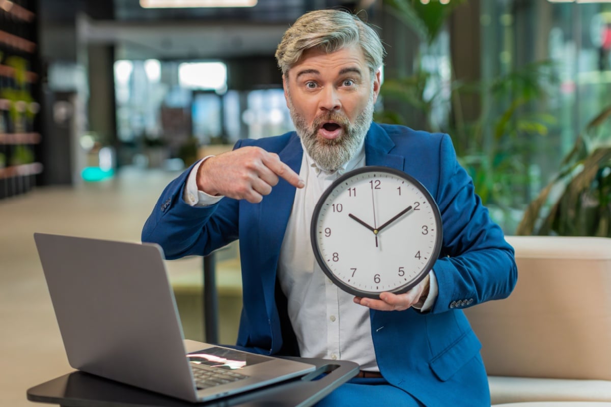 Mann zeigt auf Uhr zur Verdeutlichung einer ablaufenden Bürgergeld-Frist am Laptop.