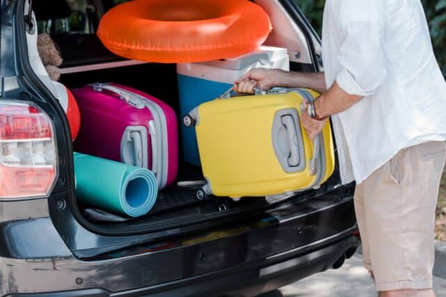 Mann lädt bunte Koffer, Isomatte und Schwimmring in den Kofferraum – Symbol für Urlaub mit Bürgergeld und notwendige Jobcenter-Zustimmung