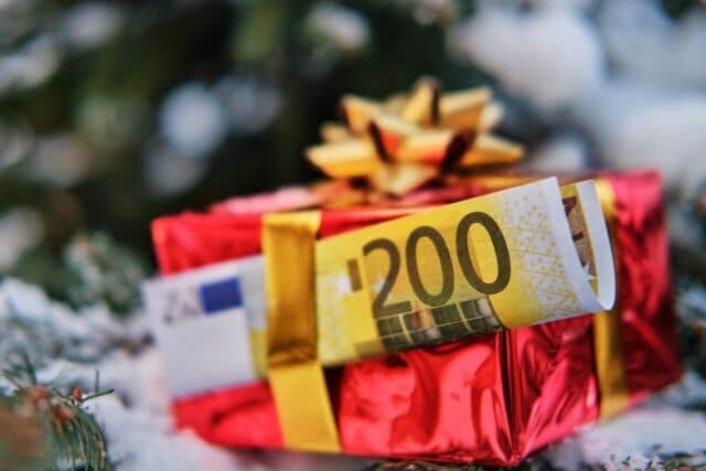 Eingepacktes Geschenk mit eingesteckten 200 Euro Schein vor einem Weihnachtsbaum