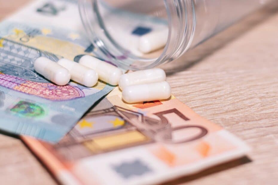 Offene Pillendose liegt auf Geldscheinen, Symbolisch für Zuzahlung zu Medikamenten