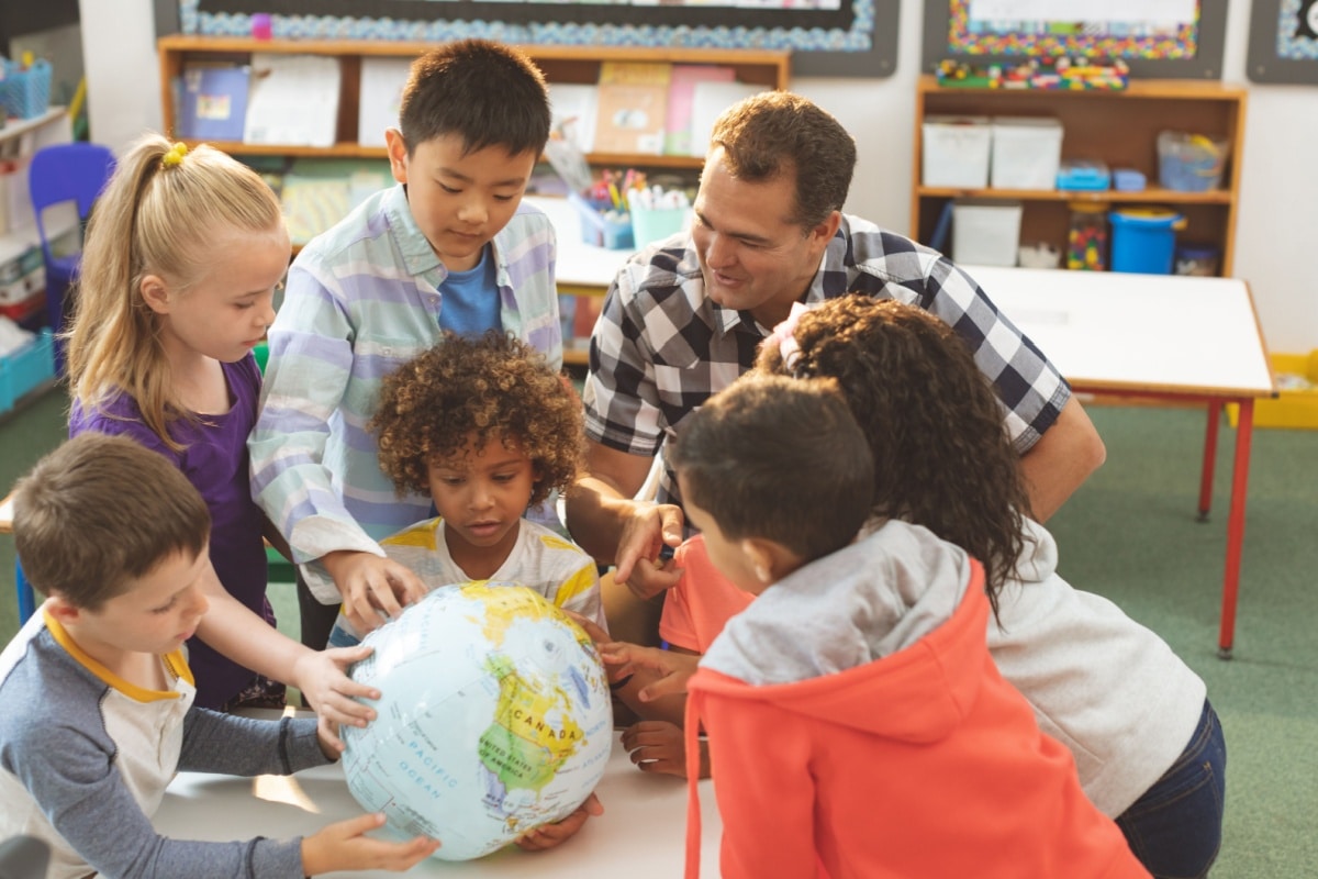 Kinder unterschiedlicher Herkunft lernen gemeinsam im Kreis um einen Globus; Symbolbild für Bildung und Teilhabe