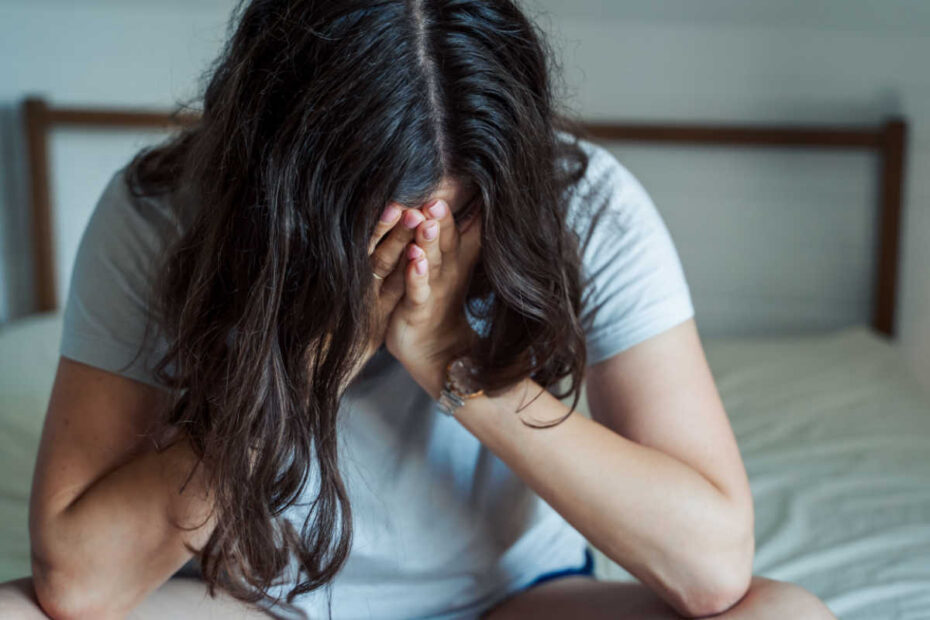 Depressive junge Frau sitzt auf Bett mit Kopf im Schoß