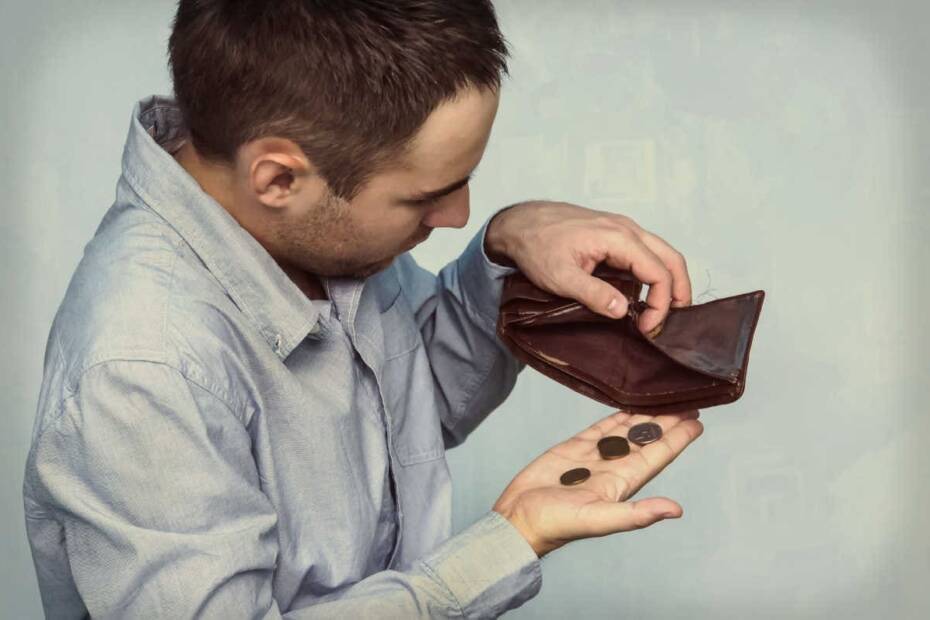 Mann guckt mit Kleingeld in leeres Portemonnaie