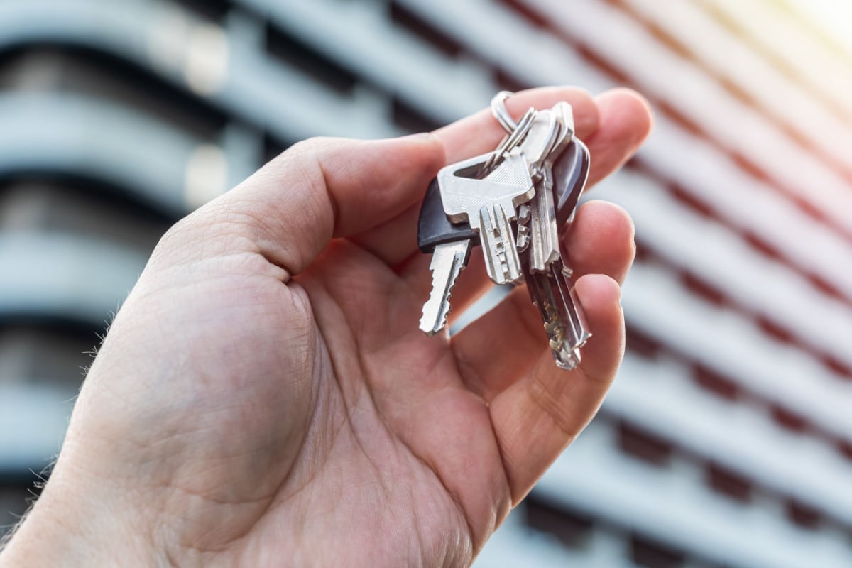 Hand hält Schlüsselbund vor neuem Wohnhaus