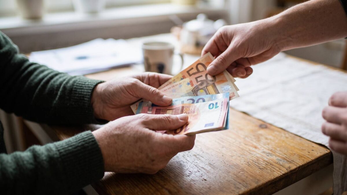 Eine Hand zieht einen 50-Euro-Schein aus dem Geldstapel einer älteren Person und veranschaulicht Abschläge bei der Erwerbsminderungsrente.