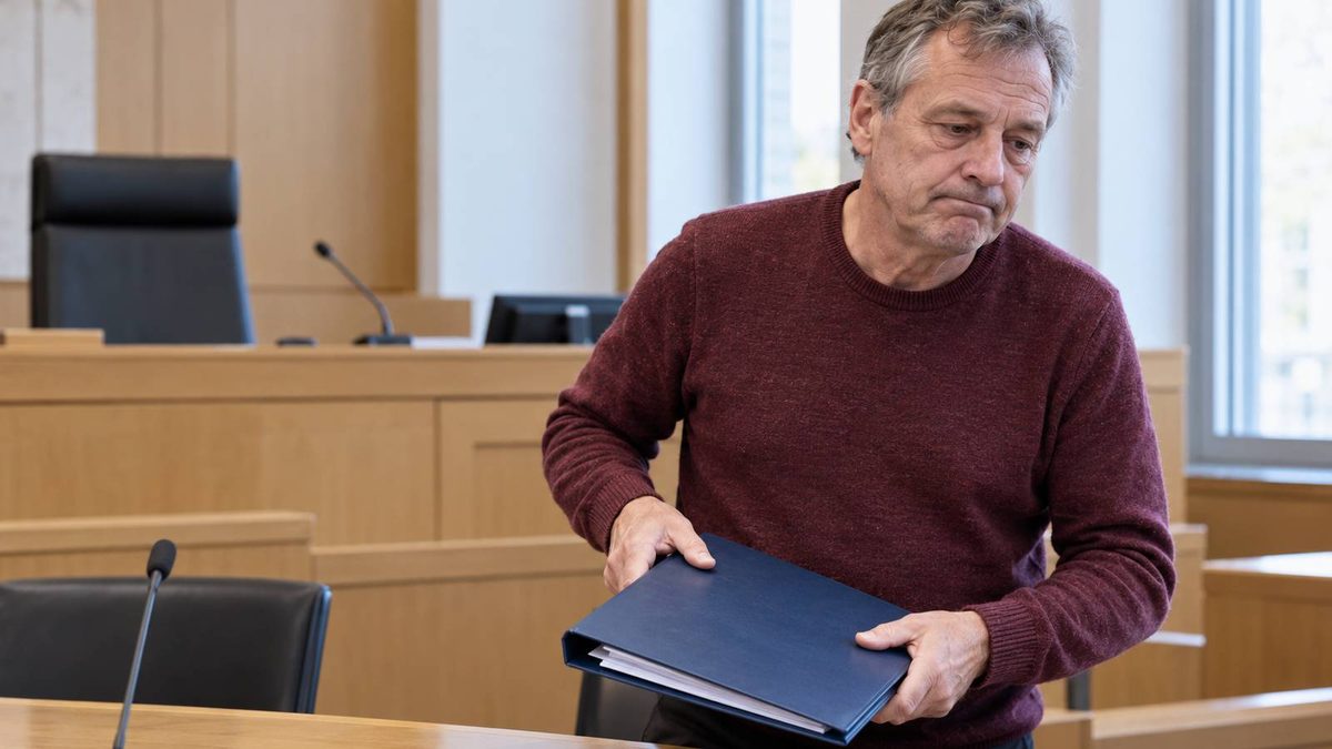 Mann mit geschlossener Aktenmappe steht an einem Tisch im Gerichtssaal.