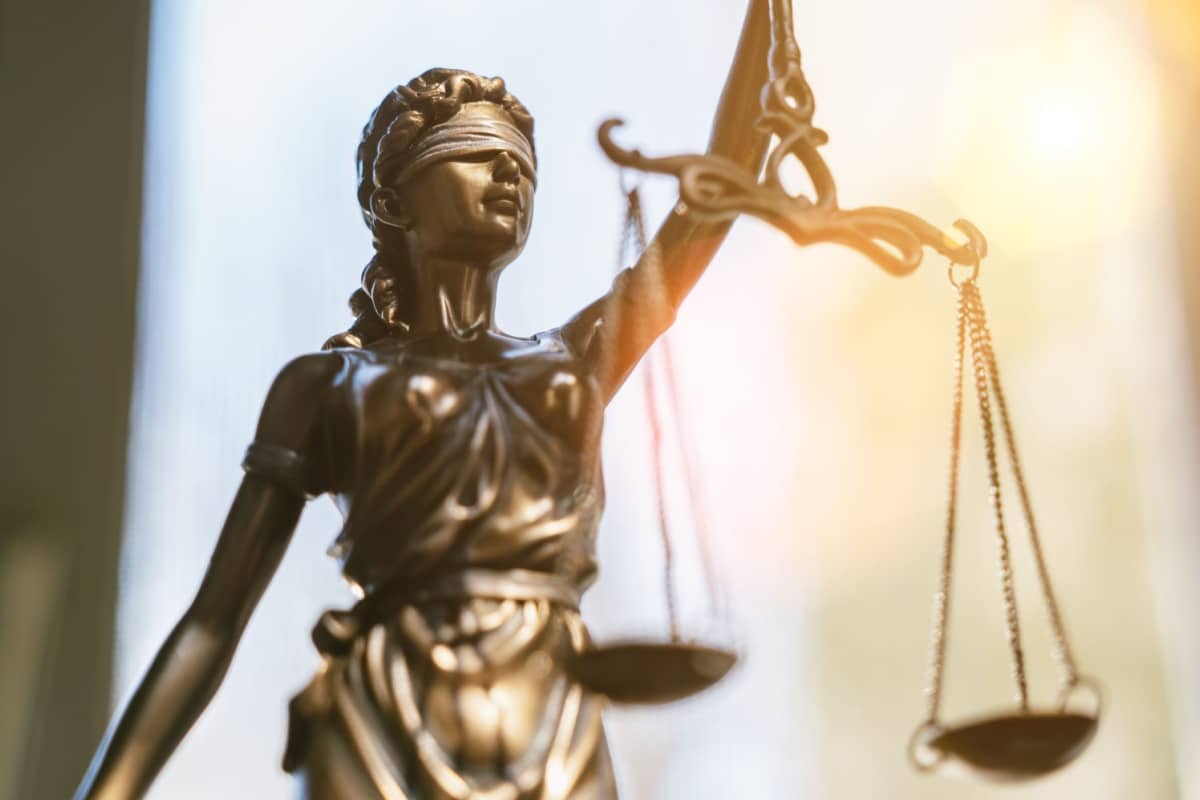 Skulptur der Justitia mit Waage in der Hand vor verschwommenem Hintergrund.
